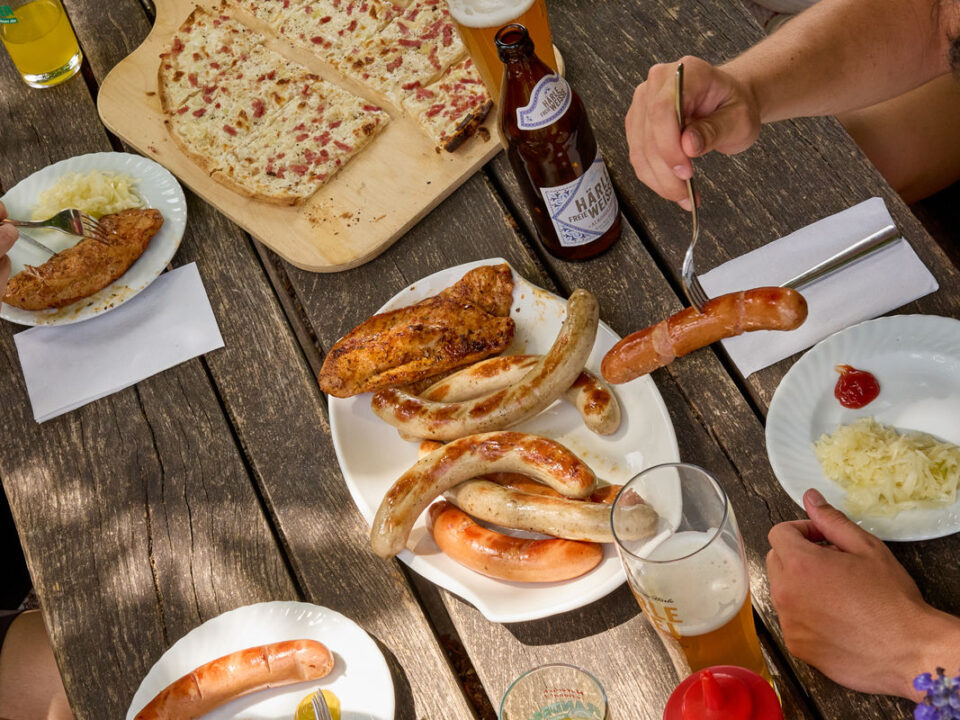 Ein reich gedeckter Tisch an Speisen frisch vom Grill und ein Flammkuchen sowie kühle Getränke.