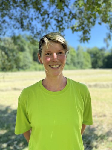 Eine Frau mit hellgrünem Shirt, die in die Kamera lächelt. Sie Mitarbeiterin.